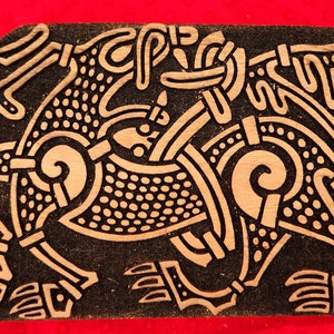 May include: A black wooden block with a detailed carving of a stylized animal with a swirling pattern. The carving is in a light brown color and has a dotted texture.