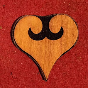 May include: A wooden heart-shaped ornament with a black mustache design.