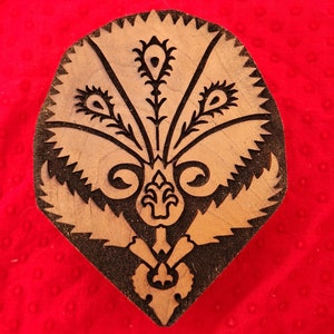 May include: A wooden printing block with a carved design of a stylized floral motif. The design is in black against a light brown wood background.