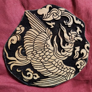 May include: A wooden carving of a phoenix with intricate details, set against a black background. The phoenix is depicted with outstretched wings and a long tail, surrounded by stylized clouds.