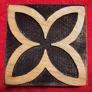 May include: A wooden square block with a carved butterfly design. The butterfly is cut out of the wood, leaving a dark brown background.