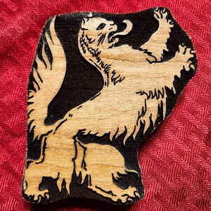May include: A wooden cutout of a black and white stylized animal, possibly a wolf or a dog, with its mouth open and teeth showing. The animal is standing on its hind legs and has its front paws raised.
