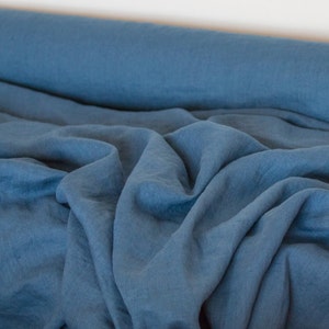 May include: A roll of blue linen fabric with a soft, textured surface. The fabric is folded and draped, showcasing its natural wrinkles and drape.