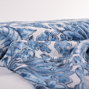 May include: A roll of fabric with a repeating blue and white pattern. The design features stylized cloud-like shapes and floral elements. The fabric is draped, showing the detailed print and texture.