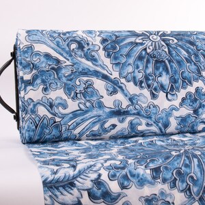 May include: A roll of fabric with a blue and white floral design. The pattern showcases large, stylized flowers and swirling cloud-like forms. The fabric is rolled and held by a black metal handle.