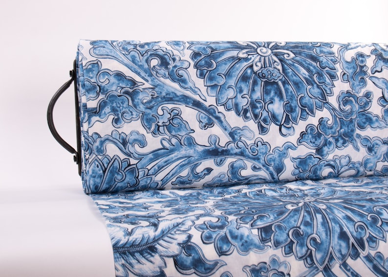 May include: A roll of fabric with a blue and white floral design. The pattern showcases large, stylized flowers and swirling cloud-like forms. The fabric is rolled and held by a black metal handle.