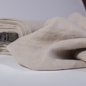 Puede incluir: Primer plano de una tela de lino beige. La tela est&aacute; doblada y drapeada, mostrando su textura y color natural.