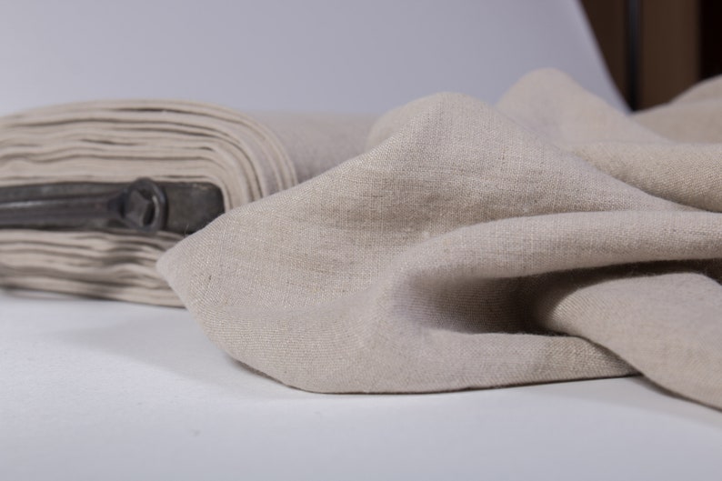 Puede incluir: Primer plano de una tela de lino beige. La tela est&aacute; doblada y drapeada, mostrando su textura y color natural.
