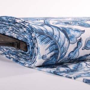 May include: A roll of fabric featuring a blue and white floral design. The fabric is rolled, displaying a pattern of stylized flowers and leaves. A black metal handle is attached to the roll of fabric.