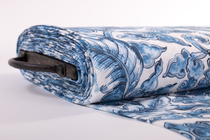 May include: A roll of fabric featuring a blue and white floral design. The fabric is rolled, displaying a pattern of stylized flowers and leaves. A black metal handle is attached to the roll of fabric.