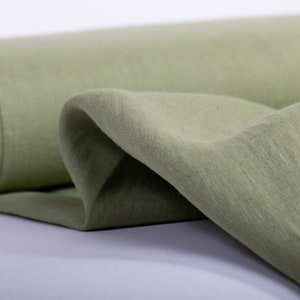 May include: A roll of soft, green linen fabric. The fabric is folded and draped, showing its texture and drape.