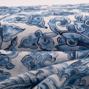 May include: Close-up of folded fabric with a repeating blue and white pattern. The design features stylized cloud and floral motifs. The fabric appears to be linen or a similar natural fibre, with a slightly textured surface.
