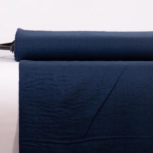 May include: A bolt of solid dark navy blue fabric rolled horizontally. The textile features a visible woven texture with a matte finish, showing a consistent deep blue color throughout the entire length of the material displayed on the roll.