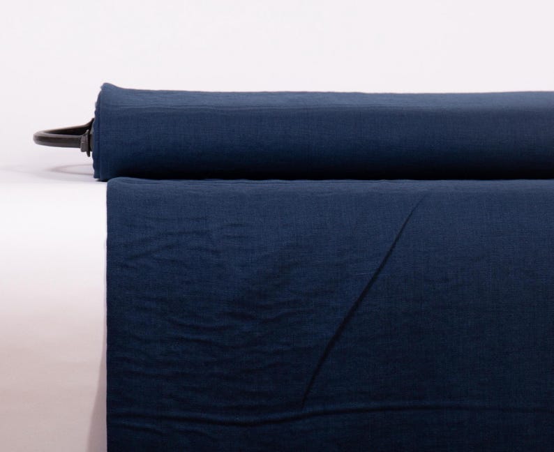 May include: A bolt of solid dark navy blue fabric rolled horizontally. The textile features a visible woven texture with a matte finish, showing a consistent deep blue color throughout the entire length of the material displayed on the roll.