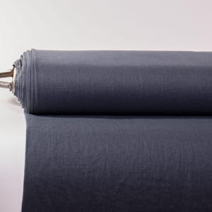 May include: A large roll of solid dark charcoal gray fabric. The textile is tightly wound around a central core, with a portion of the material unrolled and extending forward, showcasing a smooth, matte surface and a consistent, deep gray color.