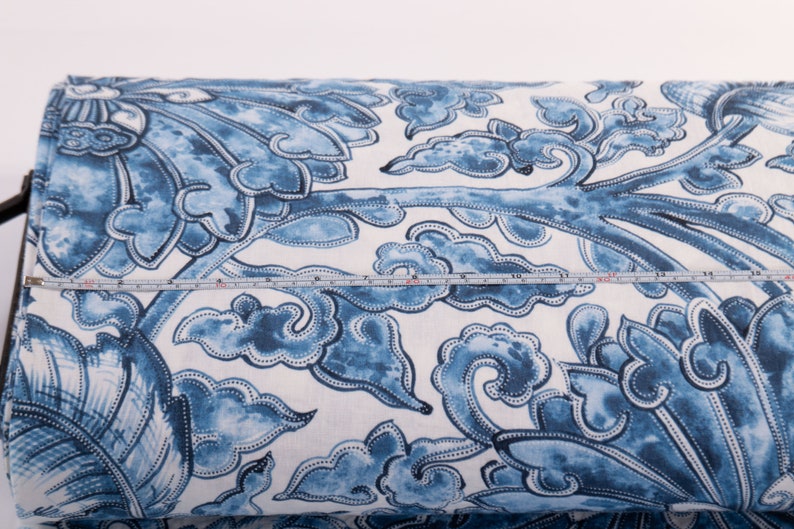 May include: A roll of fabric with a blue and white floral design. The pattern features stylized flowers and cloud motifs. A measuring tape indicates the fabric's width. The fabric is ideal for sewing and craft projects. The width is approximately 30 cm.