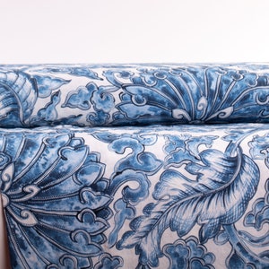 May include: Two rolls of fabric with a blue and white floral pattern. The design features large, stylized leaves and cloud-like shapes. The fabric is rolled up, showing the pattern in detail.