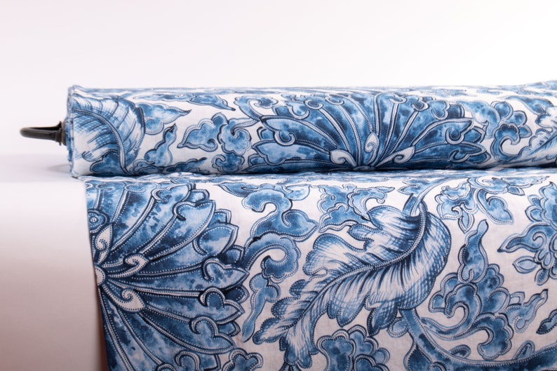 May include: Two rolls of fabric with a blue and white floral pattern. The design features large, stylized leaves and cloud-like shapes. The fabric is rolled up, showing the pattern in detail.