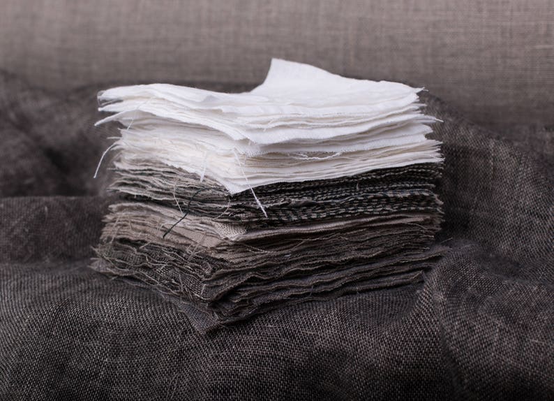 May include: A stack of fabric squares in various shades of gray and white. The fabric is soft and textured, with a slightly rough feel. The squares are arranged in a neat pile, with the white squares on top.