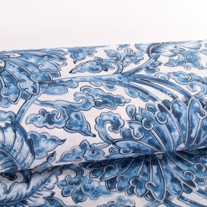 May include: A roll of fabric displaying a blue and white floral design. The pattern includes stylized flowers, leaves, and cloud motifs. The fabric is held by a black metal rod, indicating it's a bolt of material suitable for sewing or crafts.