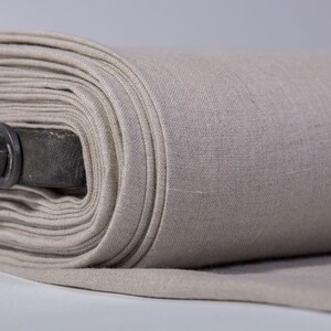 May include: A roll of beige linen fabric, tightly wound, with visible texture and a metal rod running through the center. The fabric is a neutral color, suitable for various sewing and crafting projects.