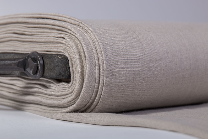May include: A roll of beige linen fabric, tightly wound, with visible texture and a metal rod running through the center. The fabric is a neutral color, suitable for various sewing and crafting projects.