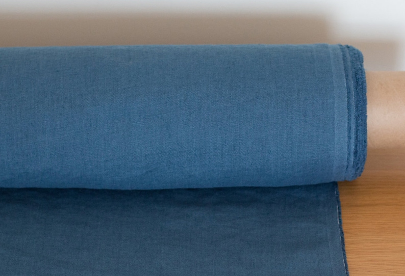 May include: A roll of blue linen fabric. The fabric has a slightly textured surface and is rolled up tightly.