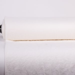 May include: A large roll of off-white fabric featuring a textured, woven surface. The material is tightly wound around a central core, with a dark brown metal handle extending from the left side of the roll to facilitate handling.