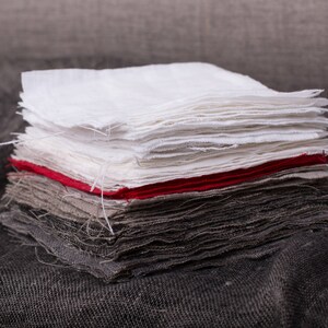 May include: A stack of fabric squares in various shades of gray, white, and red. The fabric is folded neatly and has a slightly textured surface.