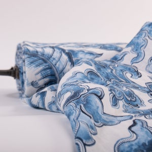 May include: A roll of fabric featuring a blue and white floral design. The fabric is unrolled, displaying a detailed pattern of stylized flowers and leaves. The roll is held by a dark brown rod.