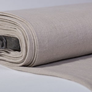 Puede incluir: Un rollo de tela de lino beige, doblado y enrollado. La tela es lisa y tiene una textura sutil.