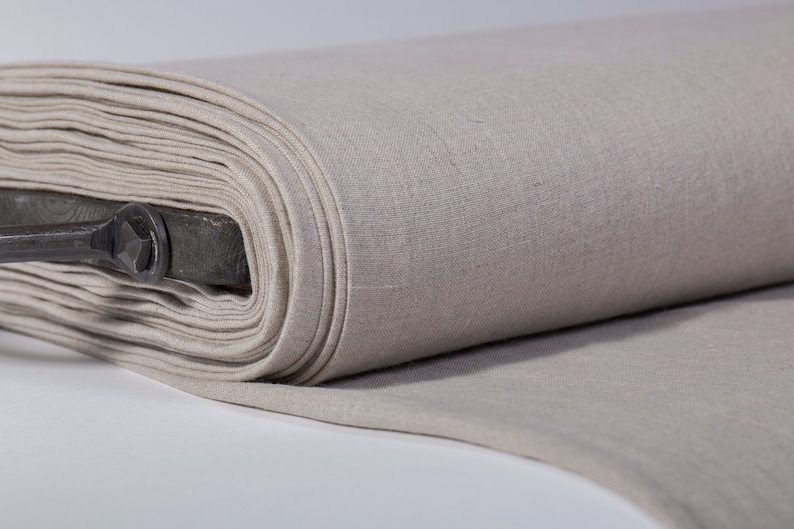 Puede incluir: Un rollo de tela de lino beige, doblado y enrollado. La tela es lisa y tiene una textura sutil.