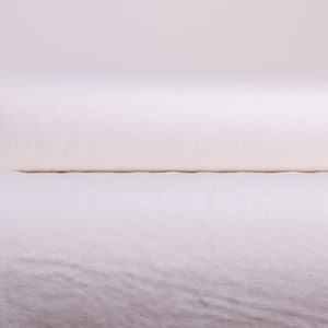 May include: A white roll of fabric is partially unrolled on a white surface. The fabric is smooth and has a slight sheen. A black metal clip is attached to the roll.