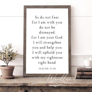 May include: A framed print with the text "So do not fear" from Isaiah 41:10. The print is in a dark wood frame and sits on a rustic wooden table. A small potted plant and books are also on the table.