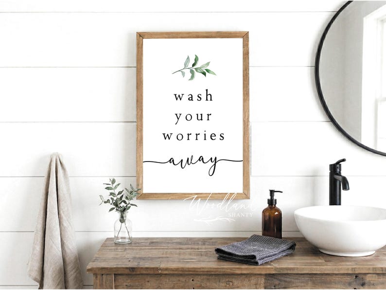 Puede incluir: Un letrero de madera enmarcado con las palabras "wash your worries away" en escritura negra. El letrero presenta una ramita de hojas verdes en acuarela. El letrero est&aacute; encima de un tocador de madera con un lavabo blanco y un grifo negro.