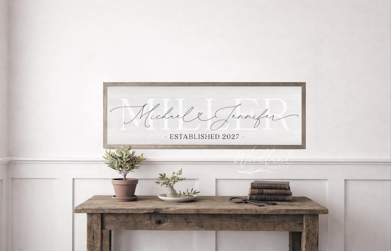 May include: A rectangular wooden wall sign with a white background and a brown frame. The sign features the large white text MILLER, the black cursive names Michael and Jennifer with a small heart, and the text ESTABLISHED 2027.