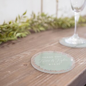 May include: A light green round coaster with the text "Thank You Jess & Tyler 8-15-23" in white lettering.