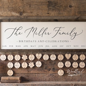 May include: A wooden family birthday and celebration sign with a framed white background and black text that reads "The Miller Family - Birthdays and Celebrations." Below are wooden tags with names and dates. A vintage lantern and vase of flowers are also present.