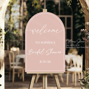 May include: A pink welcome sign on an easel, announcing "Welcome to Sophia's Bridal Shower" with the date 8/15/26. The sign is 76 cm high and 51 cm wide, with a dusty pink background. The sign is displayed outdoors.