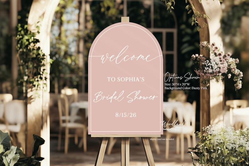 May include: A pink welcome sign on an easel, announcing "Welcome to Sophia's Bridal Shower" with the date 8/15/26. The sign is 76 cm high and 51 cm wide, with a dusty pink background. The sign is displayed outdoors.