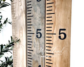 May include: A wooden growth chart with black numbers and markings. The chart is made of two different types of wood, one light and one dark. The numbers on the chart go up to 6 feet. The text "Woodland Shanty" is written on the chart.