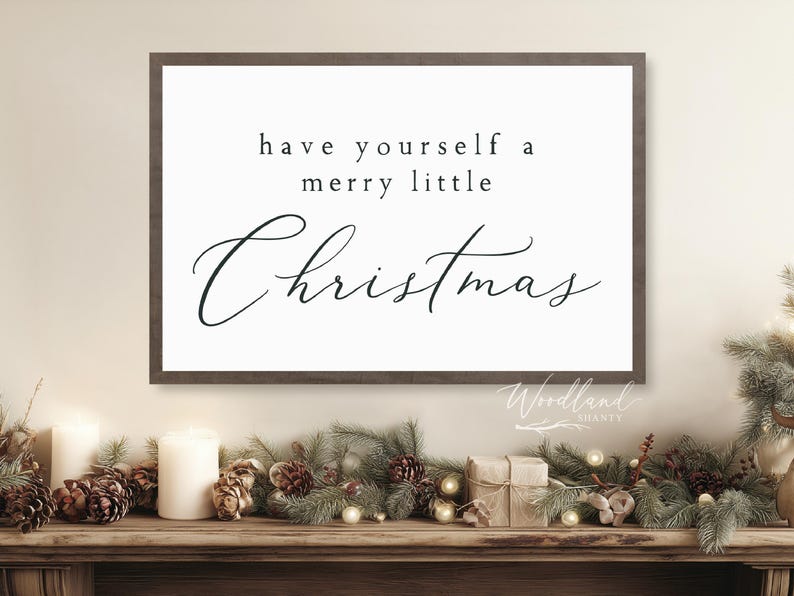 May include: A framed sign with the text "have yourself a merry little Christmas" in black script. The sign is above a wooden mantel decorated with pinecones, greenery, candles, and small wrapped gifts.