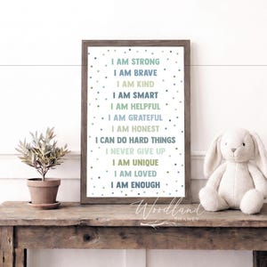 May include: A framed print with inspirational affirmations in various colors, including "I AM STRONG" and "I AM BRAVE." A plush bunny and potted plant sit on a rustic wooden table. The print has a wooden frame.