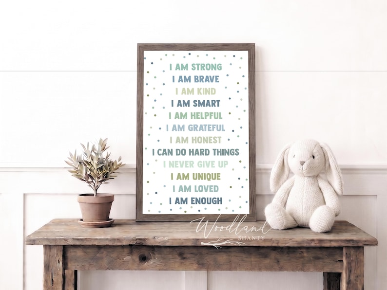 May include: A framed print with inspirational affirmations in various colors, including "I AM STRONG" and "I AM BRAVE." A plush bunny and potted plant sit on a rustic wooden table. The print has a wooden frame.