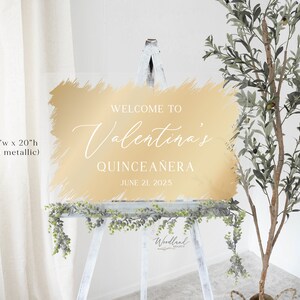 May include: Gold-colored welcome sign with a brushstroke effect, reading "Welcome to Valentina's Quincea&ntilde;era June 21, 2025". The sign is 30 inches wide by 20 inches tall.