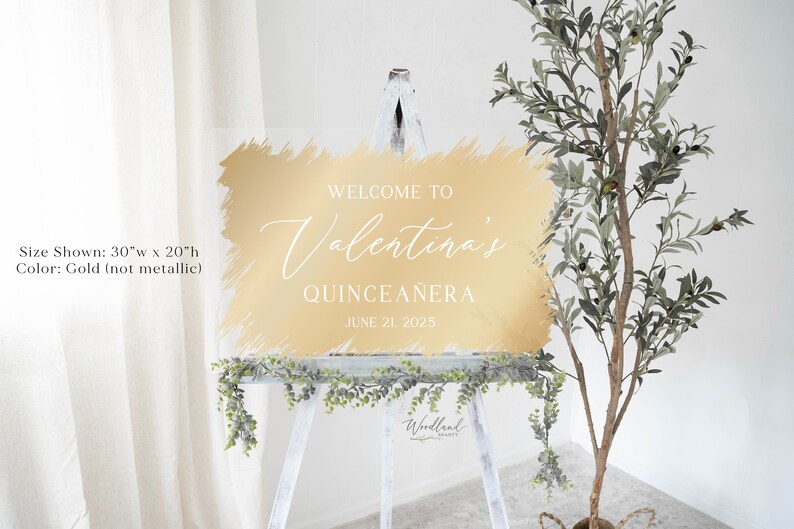 May include: Gold-colored welcome sign with a brushstroke effect, reading "Welcome to Valentina's Quincea&ntilde;era June 21, 2025". The sign is 30 inches wide by 20 inches tall.