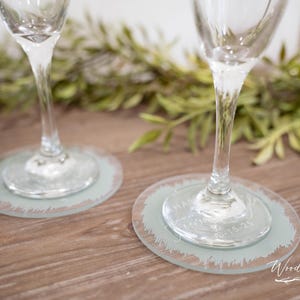 May include: Two clear glass champagne flutes with frosted glass coasters. The coasters have a distressed, brushstroke design and the text "Have a glass of something bubbly" is etched into the glass.