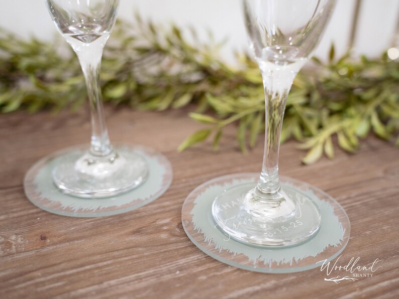 May include: Two clear glass champagne flutes with frosted glass coasters. The coasters have a distressed, brushstroke design and the text "Have a glass of something bubbly" is etched into the glass.