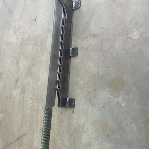 May include: A metal wall-mounted knife holder with a green paracord handle. The holder has a series of slots to hold the knife blade.