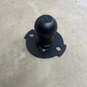 May include: A black trailer hitch ball with a round base and two mounting holes. The ball has the text "3500LB" and "F1" printed on it. The hitch is made of metal and is designed for towing.